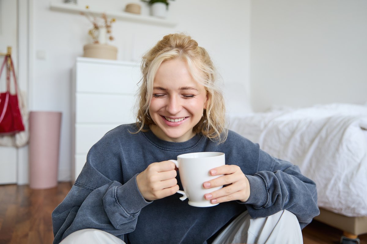 A woman smiles reassured at home, holding a mug