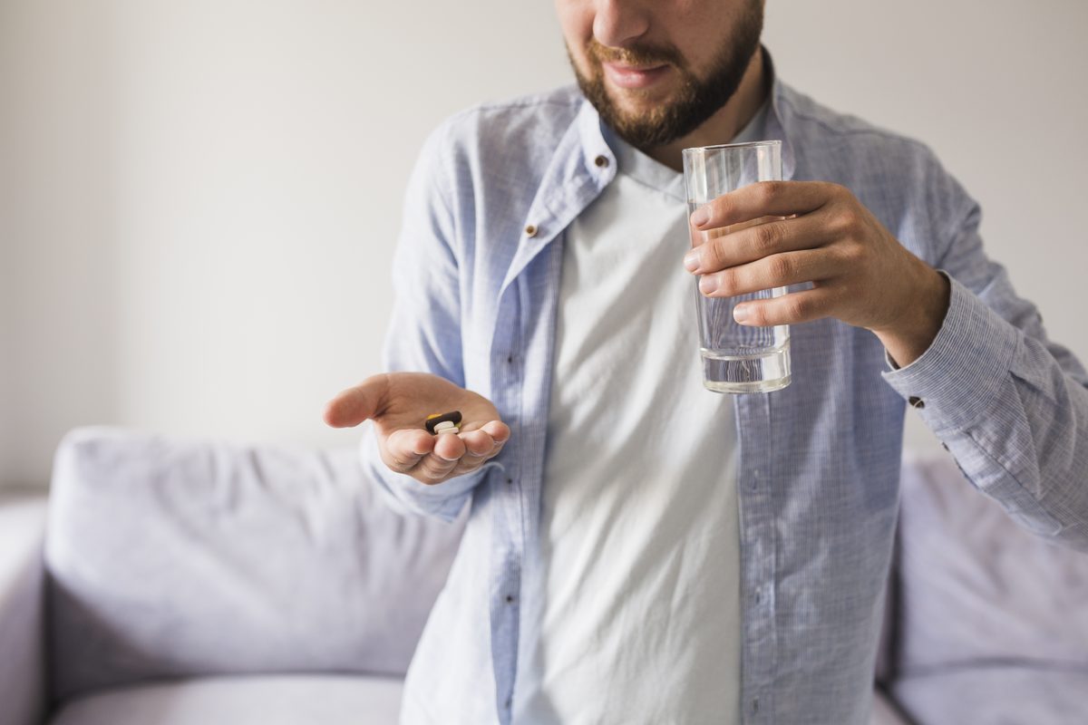 A person holding a single tablet and a glass of water at home