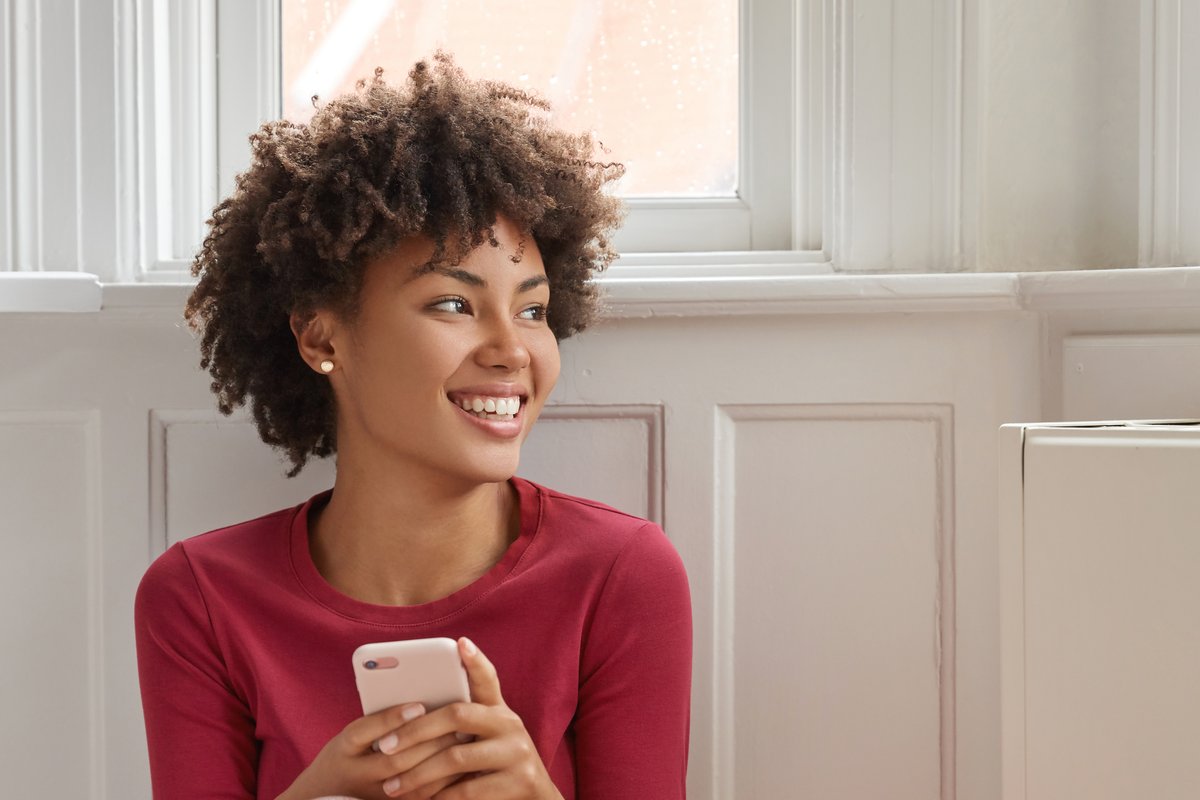 A woman reads a message on her phone at home, smiling