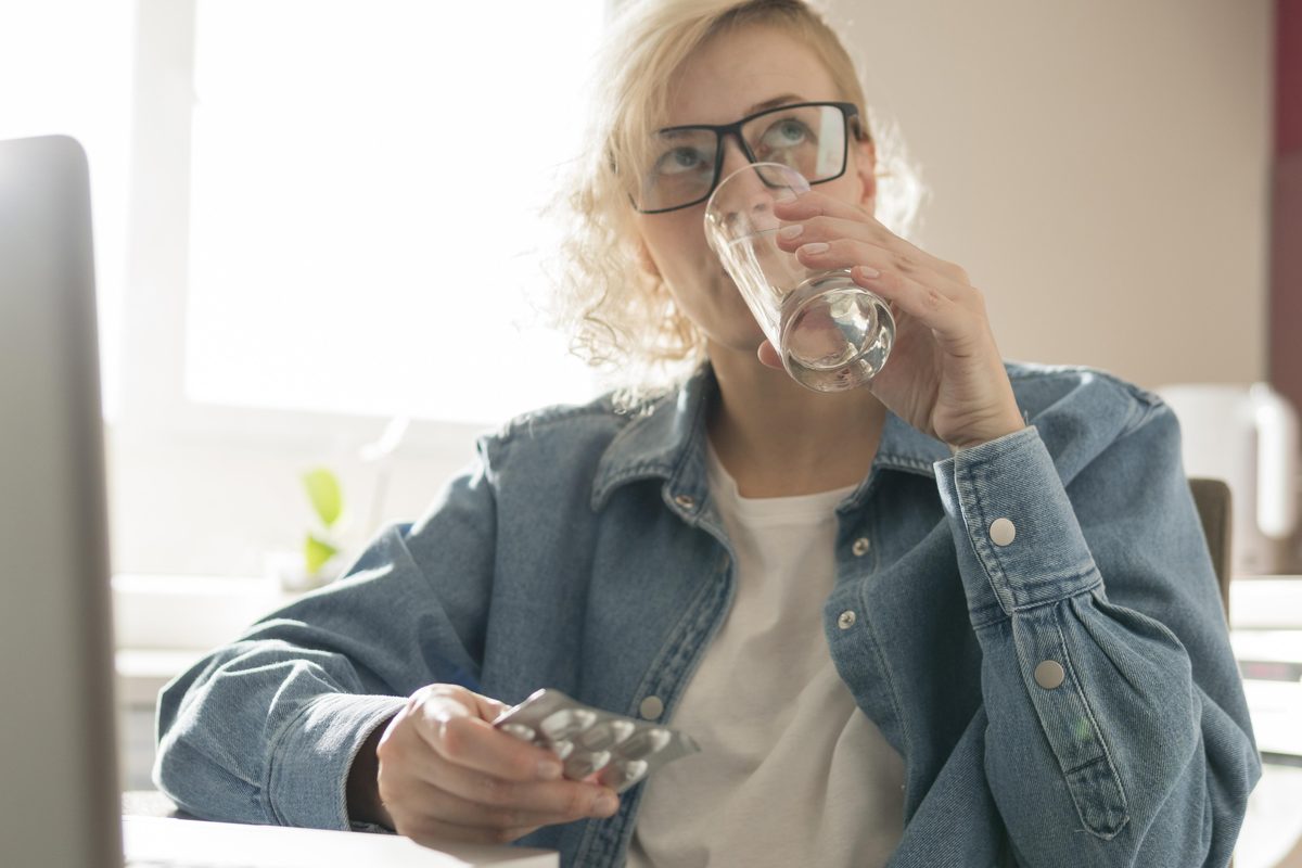 A person holding a single tablet and a glass of water at home