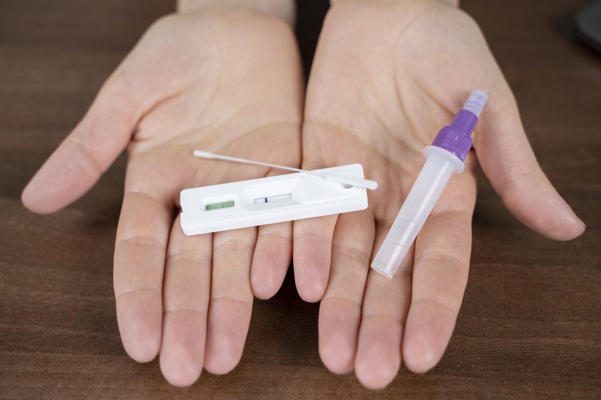 Hands holding an instant rapid test cassette and a swab collection tube